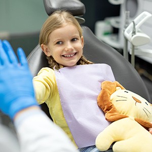 Extracted tooth resting in child’s hand Little girl high fiving her dentist