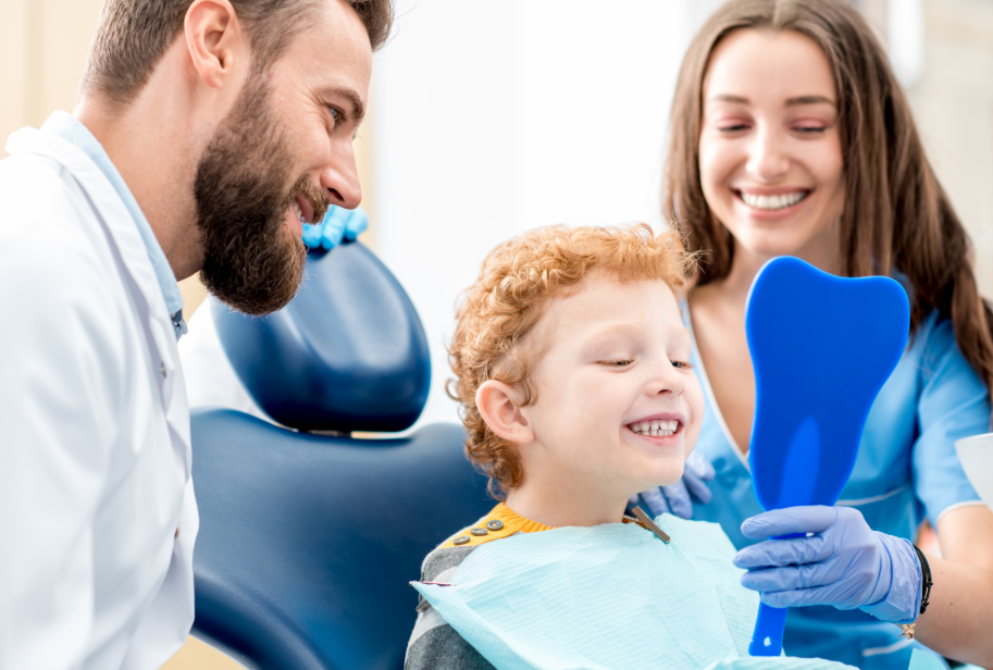 Child smiling in dental chair while dental assistant holds mirror